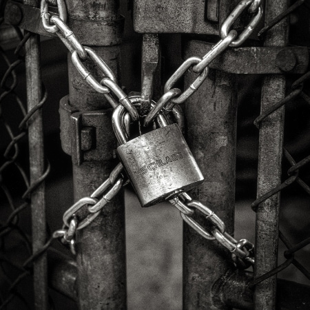 A padlock locks the chains of a rusty metal fence door