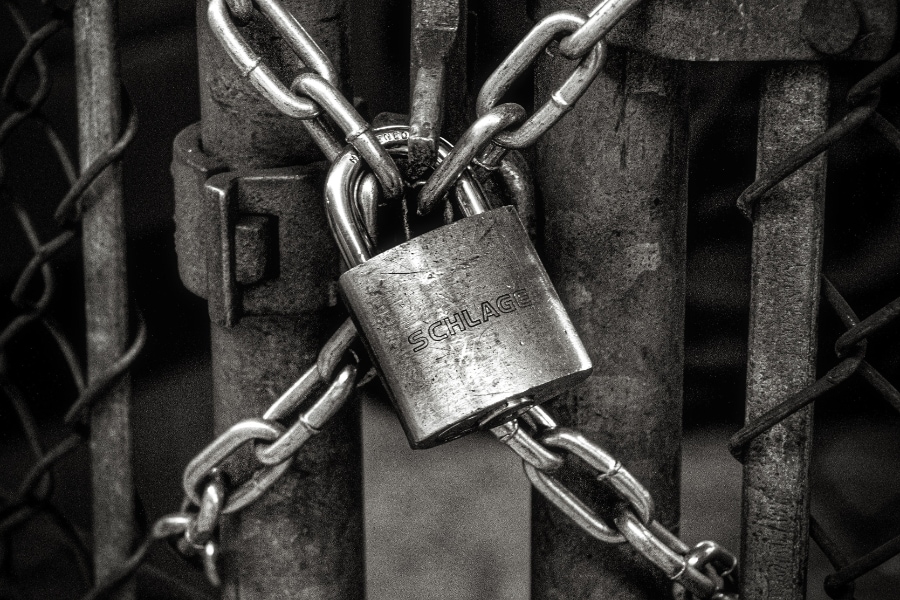 A padlock locks the chains of a rusty metal fence door