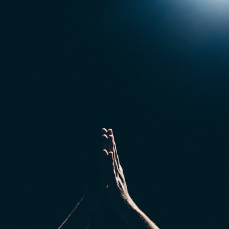 Hands clasped together up in the air in the moonlight as a person prays