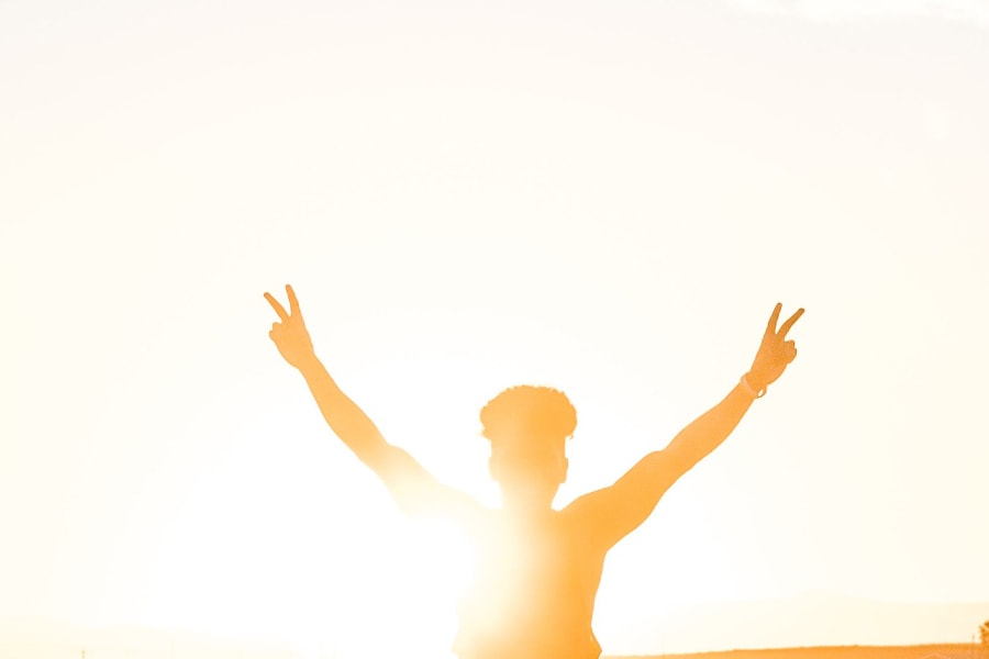 A person holding up both arms up in the air with peace signs as the sun rises behind them