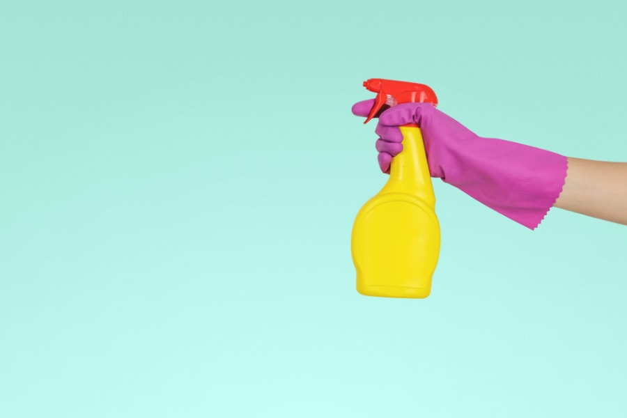 A hand in a rubber glove spraying a disinfectant solution for spring cleaning