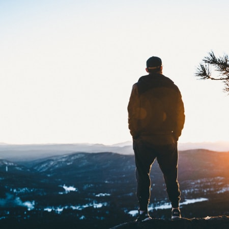 A person standing on a rock as they stare at the sun rise above the mountains