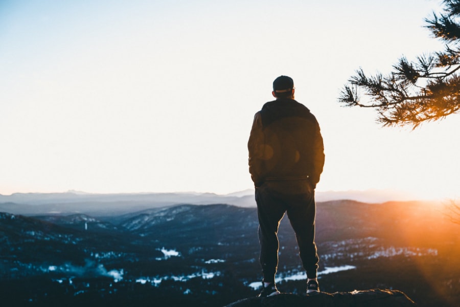 A person standing on a rock as they stare at the sun rise above the mountains