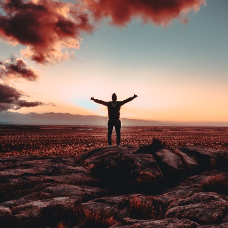 Person standing on a rock facing the sunset in the desert