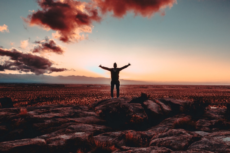 Person standing on a rock facing the sunset in the desert