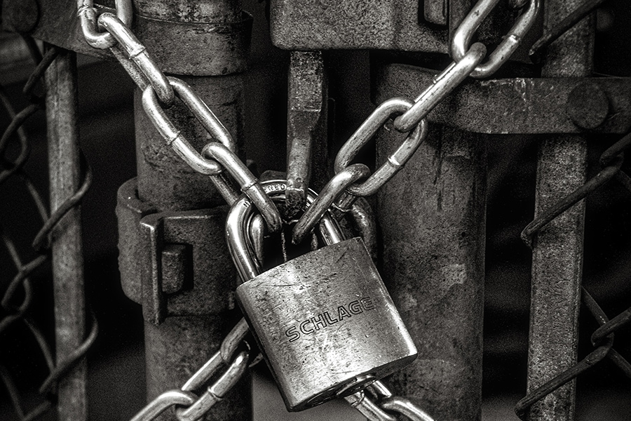 A padlock locks the chains of a rusty metal fence door