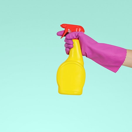 A hand in a rubber glove spraying a disinfectant solution for spring cleaning